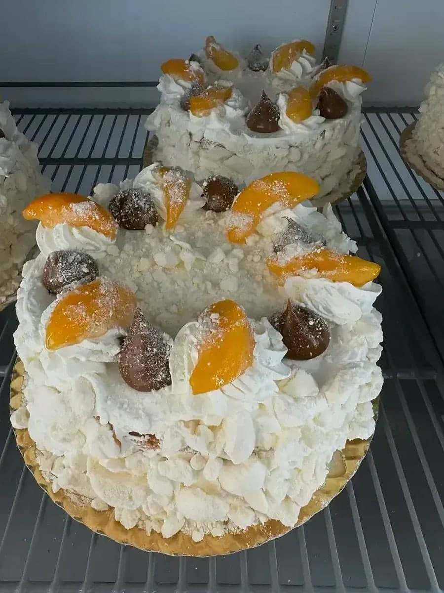 Tarta chajá de Kerrico en la vitrina, cubierta de merengue y nata con gajos de melocotón y bolitas de dulce de leche.